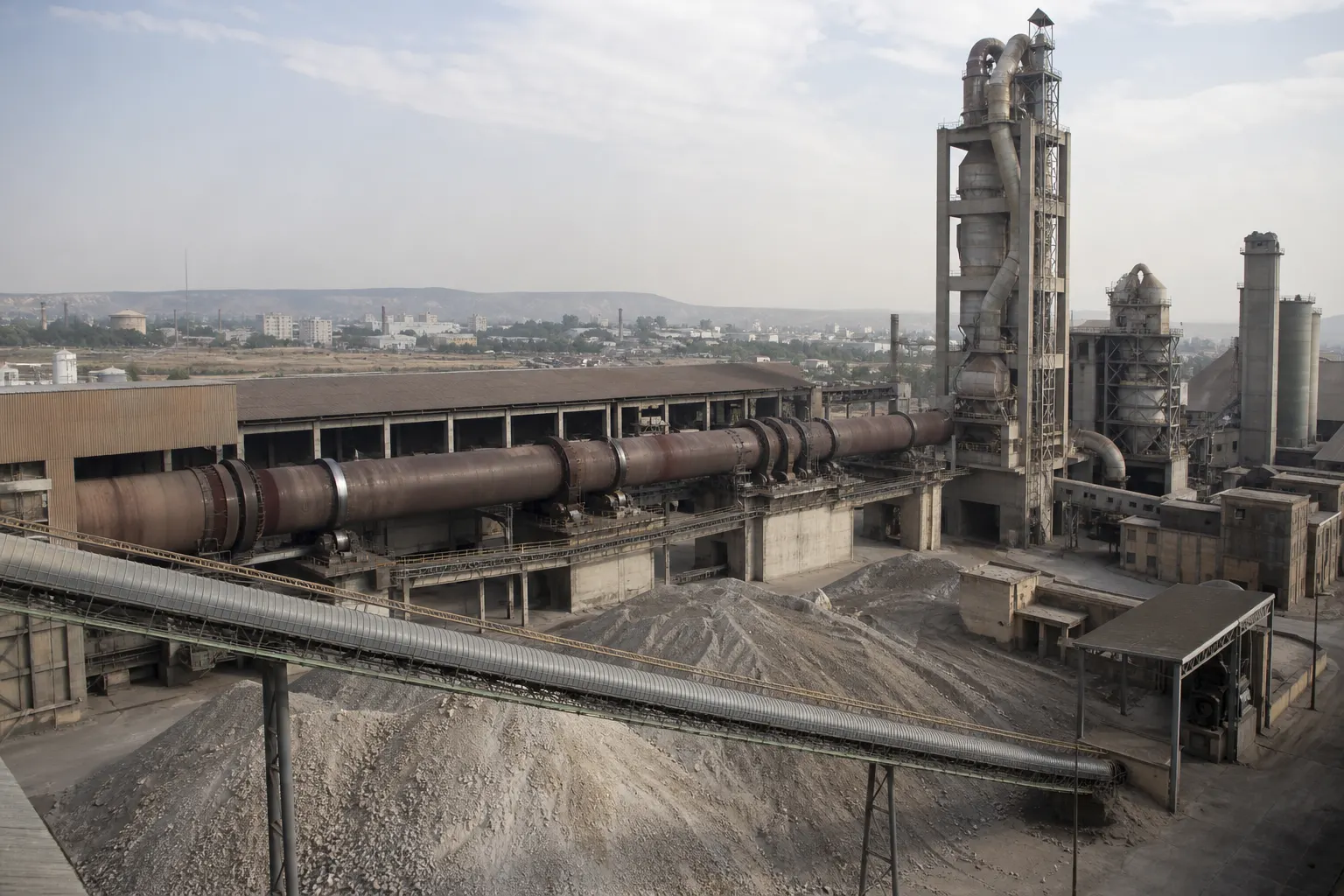 Cement plant rotary kiln, preheater tower, and limestone stockpiles