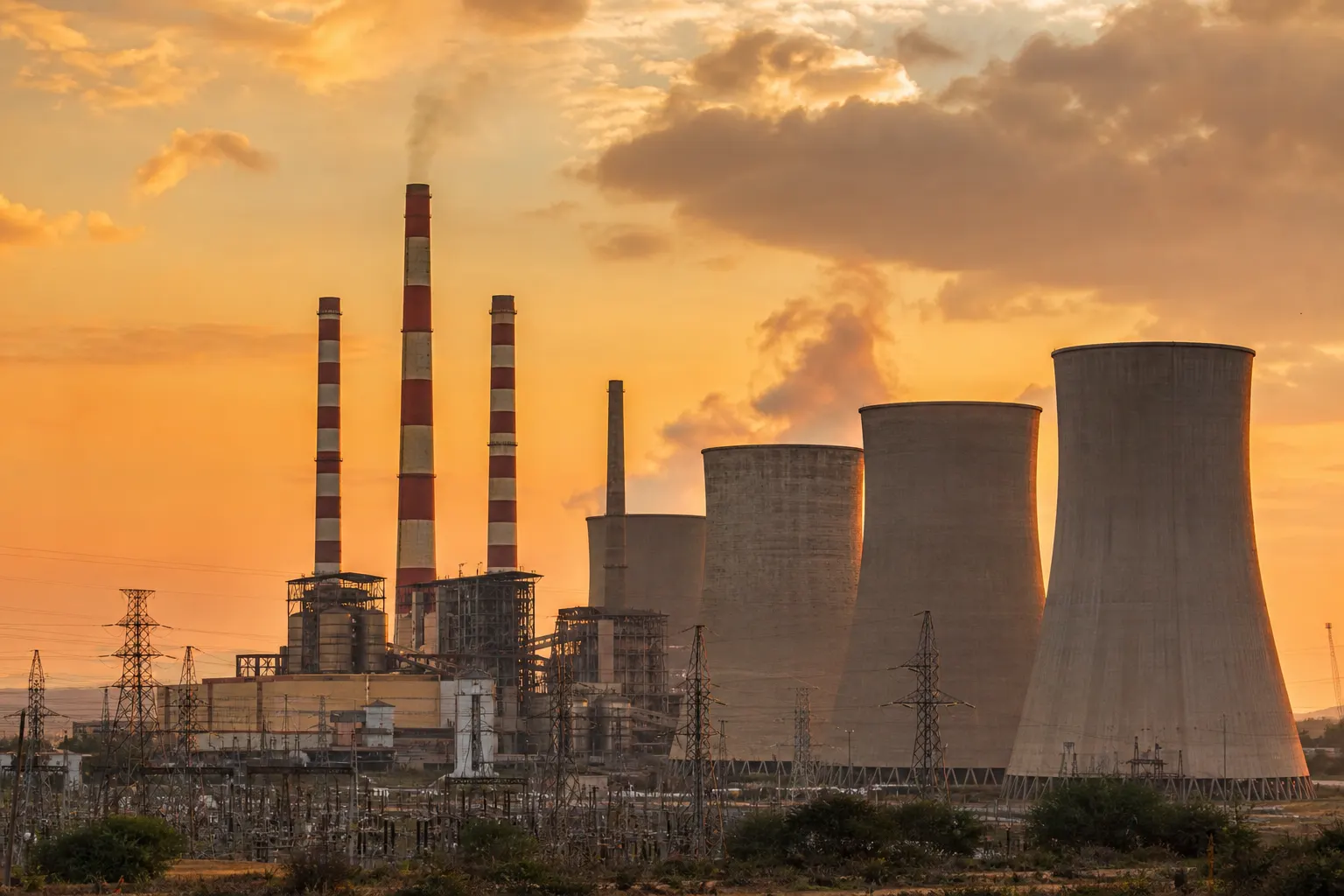 Thermal power plant with cooling towers and stack emissions at sunset